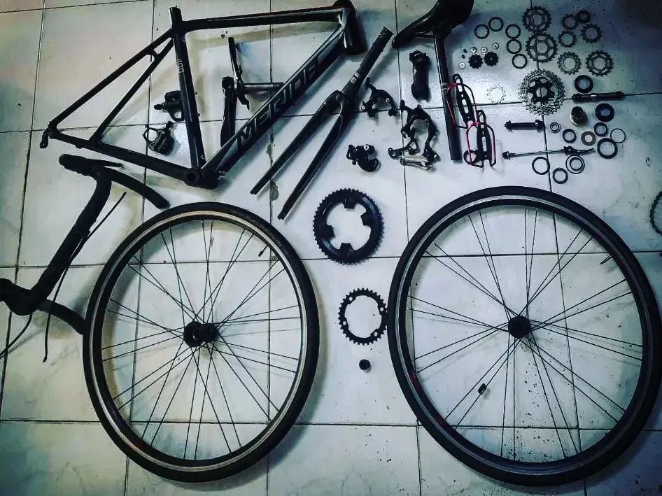 A road bike stripped down: frame, wheels, chainrings and small parts laid out on a tiled floor.