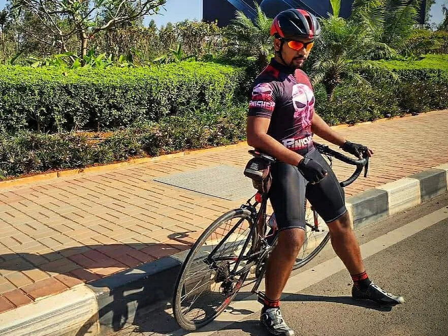 Prakash in helmet and race kit, standing astride his road bike on a sunny pavement.